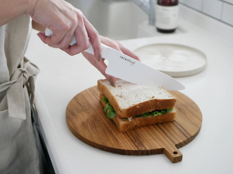 KYOCERA/京セラのココチカルナイフがまな板の上に置かれ、野菜や果物が食器に盛られたキッチン用品の配置