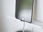 壁に取り付けられたスチール製のスマートフォン＆ヘッドホンホルダーに、スマートフォンとヘッドホンが掛けられている様子