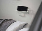 銀色のスチール製ウォールスマートフォン＆ヘッドホンホルダーが壁に取り付けられている様子。テクノロジー感のあるモダンなデザイン。