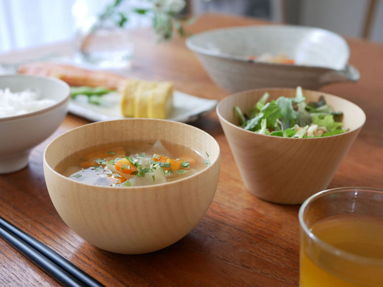 食洗機対応の天然木カップに盛られたスープと料理がテーブルに並ぶ食卓の様子