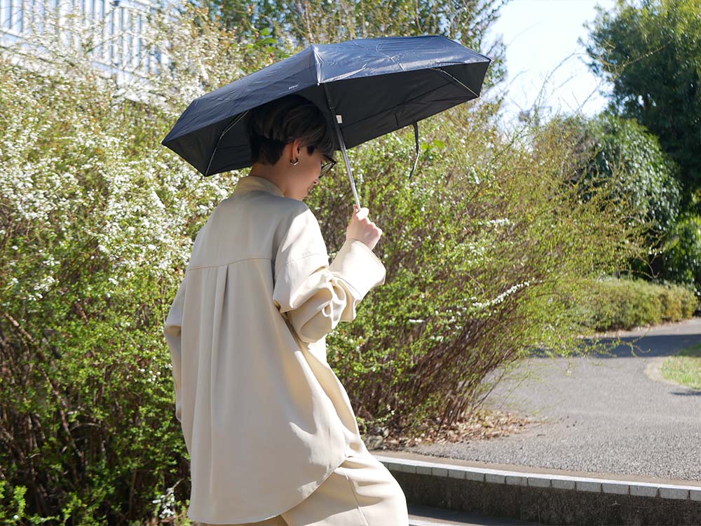 自然の中でグレーの折りたたみ傘を持ち、風や雨をしのぐ人々の様子