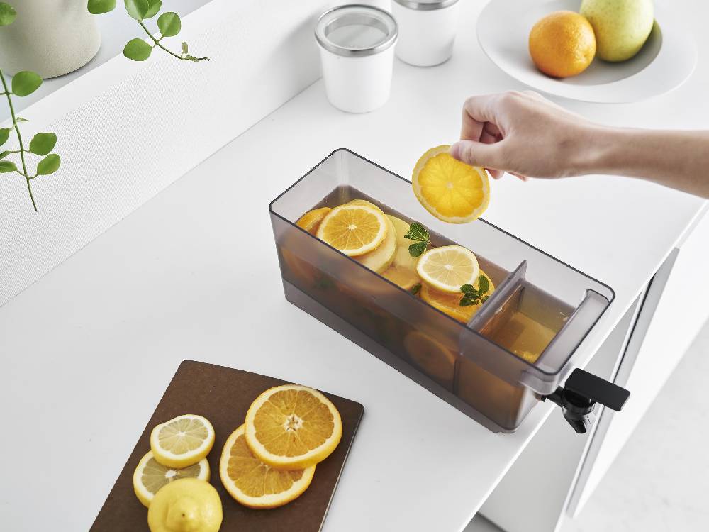 キッチンのカウンタートップに置かれた【tower/タワー】冷蔵庫ドリンクサーバーと食器、野菜が並んでいる様子