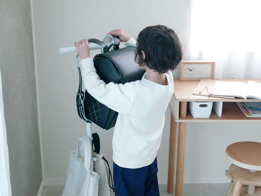幼児がスマートランドセルスタンドを使い、バッグを掛けている清潔な部屋の様子